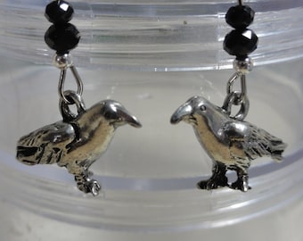 May include: A pair of silver crow earrings with black bead accents. The crows are detailed and have a realistic appearance.