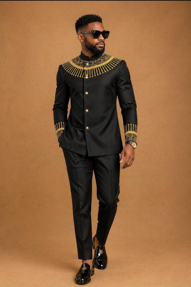 K&ouml;nnte beinhalten: Ein schwarzer Anzug bestehend aus einer Jacke mit Stehkragen, die am Ausschnitt und an den &Auml;rmelb&uuml;ndchen mit goldener Stickerei verziert ist, kombiniert mit einer passenden schwarzen Hose. Die Jacke hat eine Knopfleiste mit goldenen Kn&ouml;pfen.