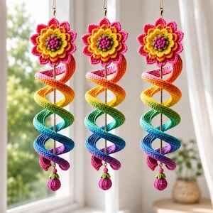 Op de afbeelding: Drie hangende haakdecoraties, elk met een levendige meerkleurige spiraalstaart die verloopt van roze naar oranje, geel, groen en blauw. Elke spiraal is bekroond met een gelaagde bloem en afgewerkt met een kleine bungelende bloemknop.