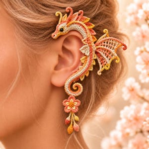 Peut inclure: Un bijou d'oreille en crochet en forme de dragon au corps long et incurvé, décliné dans des tons crème, pêche et orange. Le dragon présente des ailes détaillées, un petit œil noir et une breloque florale avec trois petits éléments en goutte.