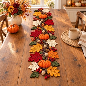 May include: A crochet table runner featuring a repeating pattern of orange pumpkins, red, yellow, green, and cream-coloured autumn leaves, small brown acorns, and clusters of red berries arranged along a dark brown vine-like central structure.