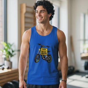 Puede incluir: Una camiseta sin mangas de color azul real con una ilustración gráfica de una bicicleta eléctrica. La bicicleta tiene un letrero de advertencia amarillo en el manillar que dice: CAUTION: BACK INJURY HAZARD RIDE SAFE, JUDGE WISE.