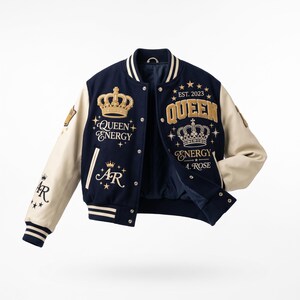 May include: A navy blue varsity jacket with cream-colored sleeves, featuring gold embroidered crowns, stars, and the text "QUEEN ENERGY", "EST. 2023", "A. ROSE", and "AR". The jacket has a snap-button front closure and striped ribbed cuffs and collar.