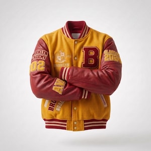 Op de afbeelding: Een varsity-jack met een mosterdgele wollen body en donkerrode leren mouwen. Het heeft een grote letter B op de borst, de tekst Brooklyn Academy en Class of 2024. Het jack is voorzien van gestreepte geribbelde boorden bij de mouwen, kraag en zoom.