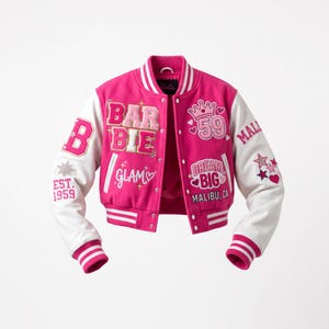 Könnte beinhalten: Eine pink-weiße Collegejacke mit gestickten Aufnähern, darunter der Schriftzug Barbie, 59, Dream Big, Malibu, CA und Glam. Die Jacke hat weiße Ärmel, eine Druckknopfleiste sowie gestreifte Rippbündchen an Ärmeln und Kragen in Pink und Weiß.