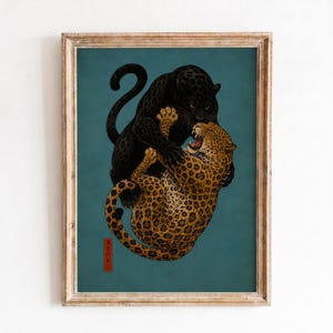 May include: A framed art print featuring a black panther and a spotted leopard engaged in a struggle against a dark teal background. The illustration includes a small red vertical rectangular stamp with black Japanese characters in the lower left corner.