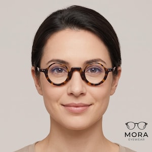 May include: Round spectacles with a tortoiseshell pattern frame. The glasses feature a keyhole bridge and two small silver-tone rivets on each side of the front frame. The text MORA EYEWEAR is printed in black below a small icon of the glasses.