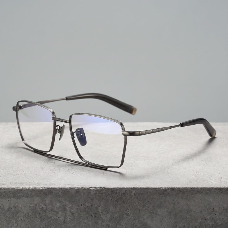 Gunmetal grey titanium frames for men, a minimalist square eyeglasses frame front view with blue light blocking clear demo lenses and adjustable metal nose pads for office glasses wear.