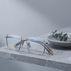 Silver titanium eyeglasses styled still life on a ceramic dish, a minimalist square optical frame for men presented as lightweight everyday glasses.