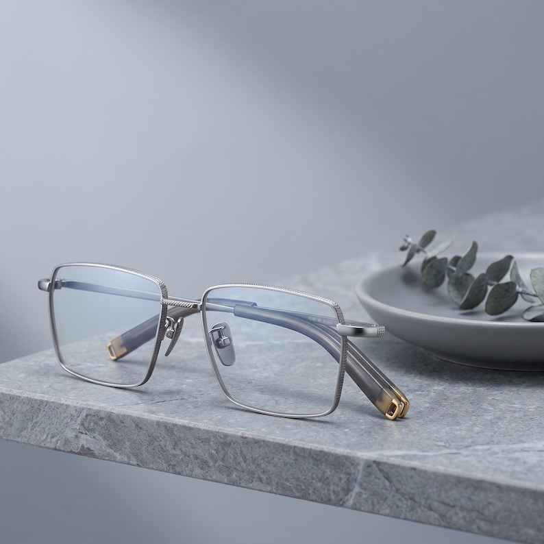 Silver titanium eyeglasses styled still life on a ceramic dish, a minimalist square optical frame for men presented as lightweight everyday glasses.