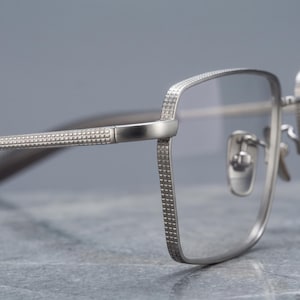 Titanium eyeglasses macro detail on a silver square optical frame, a close-up of the fine diamond-knurled cross-hatch engraving across the textured temple, rim edge and endpiece.