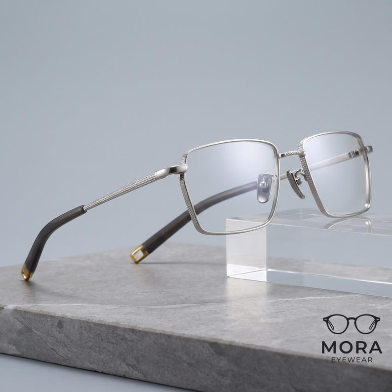 Titanium eyeglasses for men in silver, a lightweight square optical frame shown front view with clear non-prescription demo lenses and slim engraved metal temple arms for everyday business wear.