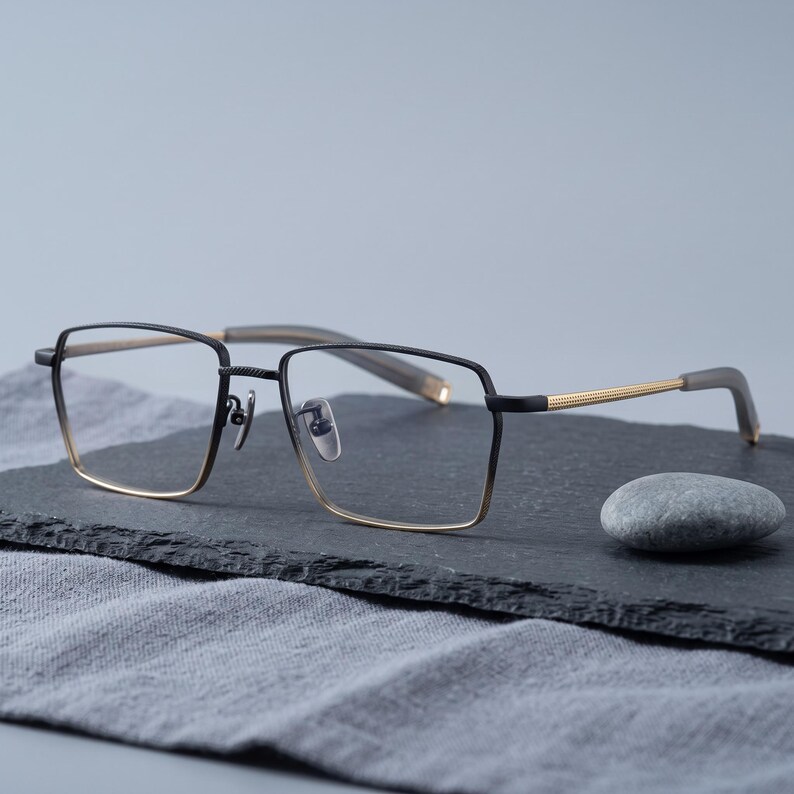 Black and gold titanium eyeglasses styled still life on natural linen, a two-tone square optical frame for men showcased as minimalist business eyewear for men.