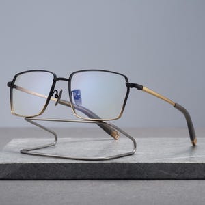 Black and gold titanium glasses for men, a two-tone square optical frame shown front view with slim metal temples and acetate tips styled as minimalist business eyewear.