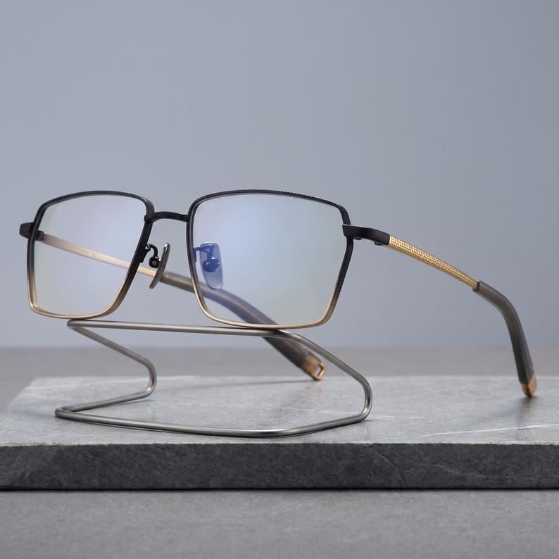 Black and gold titanium glasses for men, a two-tone square optical frame shown front view with slim metal temples and acetate tips styled as minimalist business eyewear.