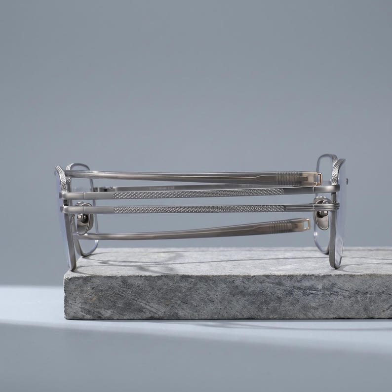 Gunmetal grey titanium frames side profile, a folded square optical frame revealing spring barrel hinges, acetate temple tips and diamond-knurled engraving along this lightweight men's eyeglasses arm.