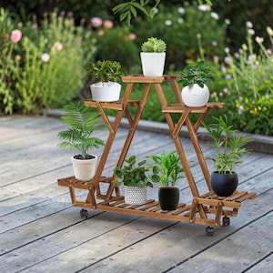 Può includere: Un supporto triangolare per piante in legno con più livelli e piccole ruote, che ospita sette piante in vaso in vari contenitori bianchi, neri e decorati. La struttura presenta un design a doghe ed è realizzata in legno tinto marrone.