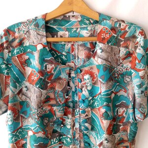 May include: A teal, brown, and red patterned blouse with a button-up front. The pattern features abstract shapes, playing cards, and faces.