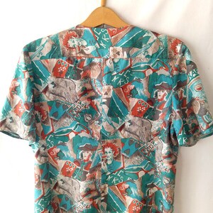 May include: A teal and brown short-sleeved blouse with a busy abstract print featuring figures, letters, and geometric shapes.
