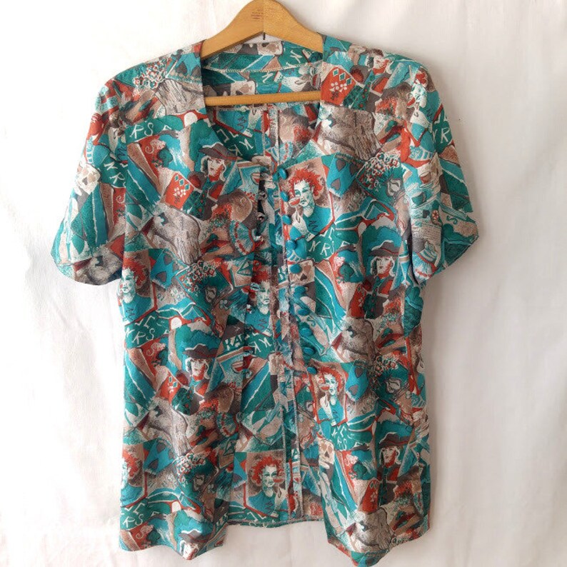 May include: A teal and orange button-up shirt with a short sleeve and a colorful abstract print. The print features various figures and patterns.