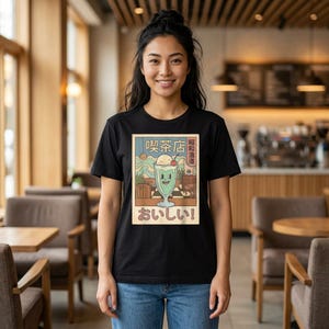 May include: A black t-shirt featuring a graphic print of a light green milkshake in a glass with a cherry on top. The design includes Japanese text that reads 喫茶店, 昭和浪漫, and おいしい, set against a background of a cafe interior.