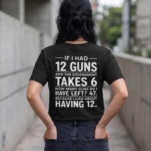 Puede incluir: Una camiseta negra de manga corta con texto blanco en la parte posterior que dice: IF I HAD 12 GUNS AND THE GOVERNMENT TAKES 6 HOW MANY GUNS DO I HAVE LEFT? 47. BECAUSE I LIED ABOUT HAVING 12. La camiseta se combina con vaqueros azul oscuro.