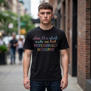 May include: A black short-sleeved t-shirt featuring the multicolored text "does this shirt make me look PROFESSIONALLY DEVELOPED?" printed on the chest. The shirt has a crew neckline and a standard fit, constructed from a solid black fabric.