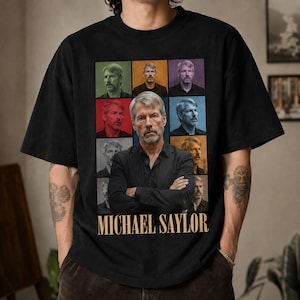 May include: A black short-sleeved t-shirt featuring a large graphic print of Michael Saylor. The design includes a central image of him with arms crossed, surrounded by eight smaller portraits in various colored squares, with his name printed below.