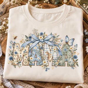 Könnte beinhalten: Ein weißes T-Shirt mit dem Wort MAMA in großen Blockbuchstaben. Die Buchstaben sind mit blauen Karomustern, Blumenmotiven und einem kleinen Hasen verziert. Über dem Text befindet sich eine große blaue Schleife, ergänzt durch einen Schmetterling und eine Biene.