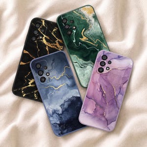 May include: Four smartphone cases featuring distinct marble and fluid ink patterns. One case is black with gold veins, one is emerald green with gold swirls, one is deep blue with gold accents, and one is a soft purple with delicate gold lines.