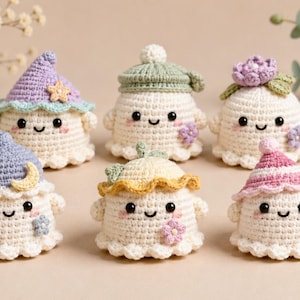 May include: Six small, cream-colored crocheted ghost figures, each wearing a unique hat. The hats feature various colors including lavender, sage green, yellow, and pink, with decorative accents like stars, moons, and flowers. Each ghost has black eyes and a stitched smile.