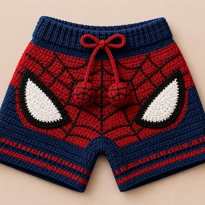 Könnte beinhalten: Gehäkelte Shorts mit einem schwarzen Spinnennetz-Muster auf rotem und blauem Grund. Die Shorts verfügen über einen gerippten Bund mit einem roten Kordelzug, der in zwei runden Bommeln endet, sowie zwei große weiße, augenförmige Applikationen.
