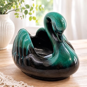 May include: A ceramic swan-shaped planter or decorative bowl featuring a glossy finish with a gradient color transition from deep black at the base to a vibrant emerald green on the upper neck and wings, showcasing a smooth, curved silhouette.