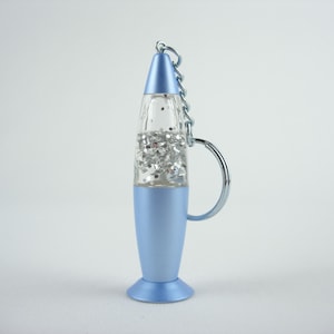 May include: A light blue lava lamp-shaped keyring with a silver chain and key ring. The clear centre contains silver glitter. The keyring is approximately 10 cm tall.