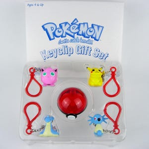 Puede incluir: Un juego de regalo de llavero Pokémon en un paquete de plástico transparente. El juego incluye cuatro llaveros de personajes, una Pokeball roja y blanca y llaveros rojos. Los personajes de Pokémon son Pikachu, Jigglypuff, Lapras y un personaje azul y amarillo.