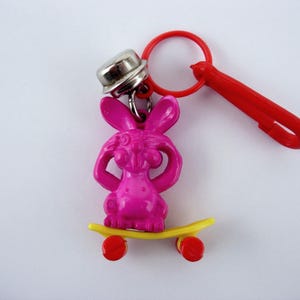 Ciondolo a forma di campanellino in plastica, autentico coniglietto da spiaggia vintage su uno skateboard, moda nostalgica degli anni '80.