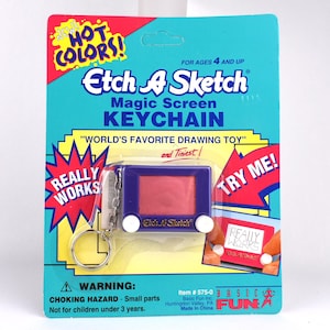 May include: A purple Etch A Sketch Magic Screen keychain in its original packaging. The card features the text "NEW! HOT COLORS!", "Etch A Sketch MAGIC SCREEN KEYCHAIN", "WORLD'S FAVORITE DRAWING TOY", "REALLY WORKS", "TRY ME!", and "WARNING: CHOKING HAZARD".