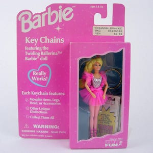 Può includere: Una confezione rosa di portachiavi Barbie con la bambola Barbie Ballerina Turbinante. La bambola indossa un tutù rosa e ha i capelli biondi. La confezione include il logo Barbie e il testo "Really Works!" e "Collect Them All."