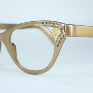 May include: Gold-toned cat-eye glasses with a floral design on the frame.