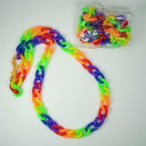 Puede incluir: Un collar de cadena de plástico de color arcoíris con un cierre dorado. El collar está hecho de eslabones ovalados entrelazados en un degradado de colores. También se ve una pequeña bolsa de eslabones de cadena a juego.
