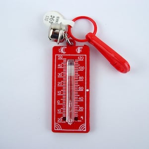 May include: A red plastic keychain with a thermometer, bell, and ring. The thermometer has a clear tube with temperature markings from 0 to 120 degrees Fahrenheit. A small tag reads "49¢".