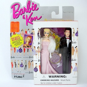 Può includere: Un set di bambole Barbie e Ken in una confezione di plastica. Le bambole sono vestite con abiti rosa e neri. La confezione ha un'etichetta di avvertenza che dice "RISCHIO DI SOFFOCAMENTO - Pezzi piccoli. Non adatto a bambini di età inferiore a 3 anni."