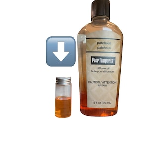 May include: A large clear plastic bottle of Pier 1 Imports patchouli diffuser oil with a black cap, labeled 16 fl oz (473 mL), alongside a small clear glass vial with a silver cap containing orange liquid, and a blue square icon with a white arrow.