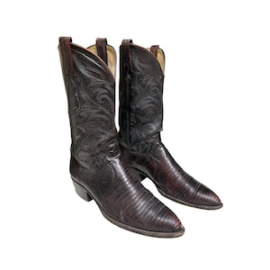 Puede incluir: Un par de botas vaqueras de cuero marrón oscuro con punta afilada, tacón de bloque y un patrón texturizado de piel de lagarto en el empeine. Las cañas altas están decoradas con intrincadas costuras tonales en espiral y tiradores.