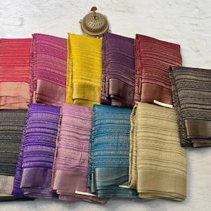 May include: A collection of eleven folded rectangular fabrics in various colors including red, pink, yellow, purple, maroon, black, blue, and gold. Each fabric features a consistent horizontal striped pattern and a wide, textured border.