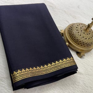 May include: A folded dark navy blue fabric textile featuring a decorative gold metallic border with a repeating floral pattern along the bottom edge, accompanied by a small, ornate, perforated brass incense burner with a finial top.