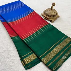 May include: A folded textile featuring horizontal bands of blue, red, and green, accented with thin gold stripes and a decorative gold geometric border pattern along the edge, accompanied by a small, ornate, perforated brass incense burner.
