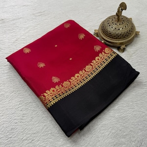 May include: A folded red saree featuring small gold floral motifs scattered across the fabric, finished with a wide gold decorative border and a solid black hem. Beside the fabric sits a round, ornate, perforated brass incense burner.