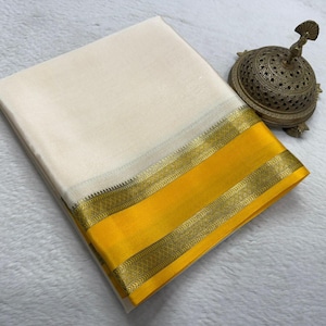 May include: A folded off-white textile with a wide yellow border and intricate gold metallic trim, accompanied by a small, ornate, dome-shaped brass incense burner featuring detailed cut-out patterns and a decorative finial on top.