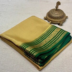 May include: A folded gold-colored fabric with a wide, deep green border featuring an intricate gold metallic floral pattern. Beside the fabric sits a small, ornate, dome-shaped brass incense burner with a perforated lid and a bird finial.